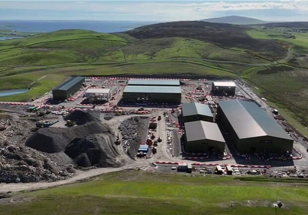 Aerial view of the Finstown Substation construction site showing large industrial buildings, earthworks, and surrounding rolling green hills in Orkney.